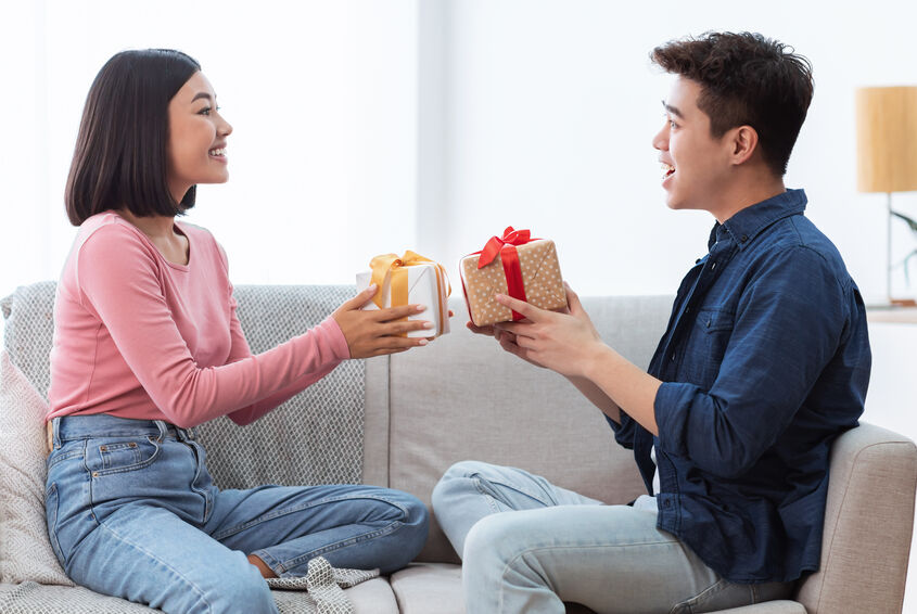 Two people sitting on a couch exchanging gifts